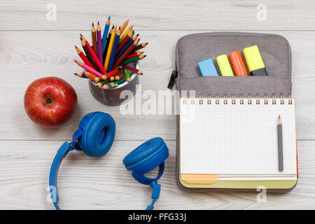 Kopfhörer, Apple, Metall Glas mit Buntstifte und offenen Übungsbuch auf Tasche - Federmäppchen mit Farbe filzstifte und Marker auf grau Holzbretter. Top Stockfoto