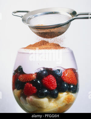 Besprengung Schokolade Pulver auf dem Rahm Auffüllen einer Frucht ricotta Tiramisu Dessert in einem Glas Wein serviert. Stockfoto