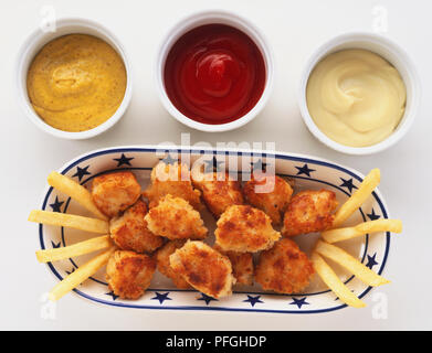 Oben Ansicht von Chicken Nuggets, gemacht mit Huhn beschichtet in breadcrumb Teig, auf Fach, mit Pommes mit Ketchup, Mayonnaise und Senf zum Dippen. Stockfoto