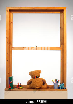 Rückansicht eines Teddybären sitzen auf der Türschiene einen Fensterrahmen, durch Spielzeug umgeben, Stockfoto