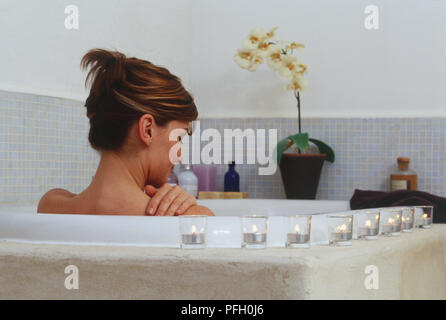 Kopf und Schultern der Frau in der Badewanne sitzend, von Kerzen, Rückansicht umgeben Stockfoto