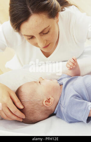 Frau beugte sich über Baby Mädchen auf dem Rücken liegend Stockfoto