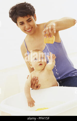 Lächelnde Frau liegt auf dem vorderen umarmten Kissen, baby boy lehnte sich auf gestapelten Kissen, Seitenansicht Stockfoto