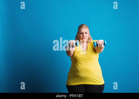 Portrait eines unglücklichen übergewichtige Frau mit Hanteln in den Händen. Studio shot auf blauem Hintergrund. Kopieren Sie Platz. Stockfoto