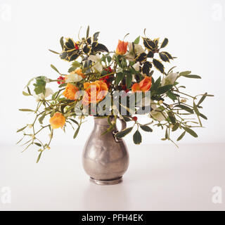 Orange Rosen, weissen Zuckererbsen, Holly Blätter und Beeren in eine Vase arrangiert, Seitenansicht Stockfoto