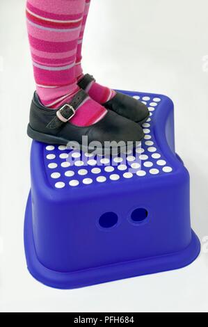 Child's Beine und Füße, tragen rosa Gestreifte Strumpfhosen und schwarze Schuhe, stehend auf Plastik Schemel, close-up Stockfoto