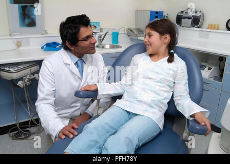 Zahnarzt crouching neben Mädchen im Zahnarztstuhl Stockfoto
