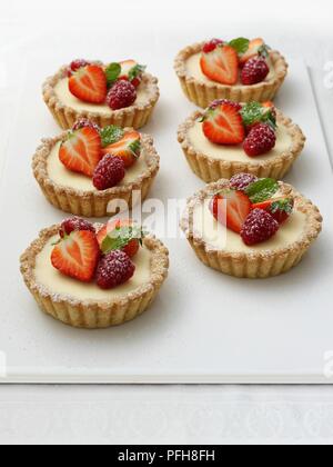 Weiße Schokolade und mascarpone Törtchen, mit Erdbeeren, Himbeeren und Minze dekoriert, close-up Stockfoto