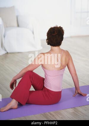 Frau auf einer Matte sitzen, ein Bein über das andere Bein gefaltet, Weg suchen, Ansicht von hinten Stockfoto