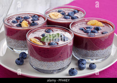 In der Nähe von köstlichen 2-in-1-Smoothie mit Blaubeeren, Chia Samen Mousse und Banane in Gläsern auf Platte auf Holz- Tabelle, Ansicht von oben Stockfoto