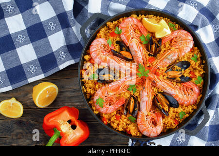 Köstliche Meeresfrüchte Valencia Paella mit Gambas, Muscheln auf herzhafte cremige Safran Reis mit Gewürzen und Zitrone Keile in der Wanne, auf hölzernen Tisch, Blick f Stockfoto