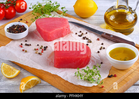 Köstlich frischen, rohen Thunfisch Steaks für Kochen auf Schneidebrett mit Thymian, Zitrone Schichten vorbereitet. Olivenöl und Kirschtomaten auf backgroun Stockfoto