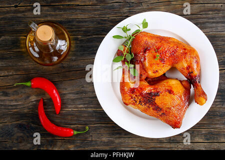 Brathähnchen bein Viertel mit knusprigen goldbraunen Haut mit frischem Grün Thymian auf weiße Platte auf dunklem Holz mit Chili Peppers und b Stockfoto