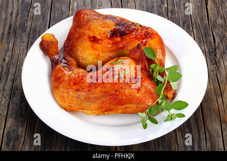 Brathähnchen bein Viertel mit knusprigen goldbraunen Haut mit frischem Grün Thymian auf weiße Platte auf dunklen Holzbrettern, Ansicht von oben, Schließen - Stockfoto