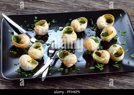 Köstliches Gericht - Schnecken de Bourgogne oder Schnecken mit Kräuter Butter Knoblauch bestreut mit fein gehackter Petersilie auf schwarze Platte mit Schnecke für Stockfoto