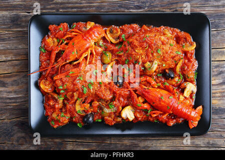 Huhn Marengo - lecker Hühnerfleisch Eintopf mit crawfishies, gehackte Tomaten, Zwiebeln, Champignons und Oliven auf schwarze Platte auf alten Holztisch, Authen. Stockfoto