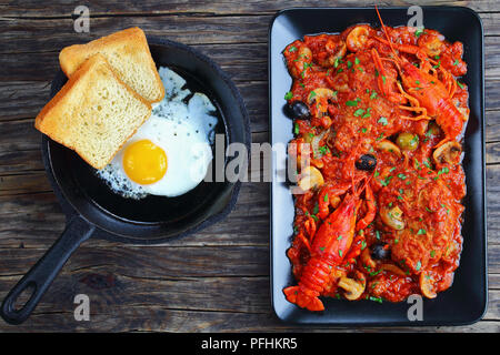 Huhn Marengo - lecker Hühnerfleisch Eintopf mit crawfishies, gehackte Tomaten, Zwiebeln, Champignons und Oliven auf schwarze Platte, Toast und sunny side up f Stockfoto