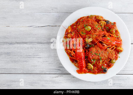 Huhn Marengo - lecker Hühnerfleisch Eintopf mit crawfishies, gehackte Tomaten, Zwiebeln, Champignons und Oliven auf weiße Platte auf alten hölzernen Tisch, Blick f Stockfoto