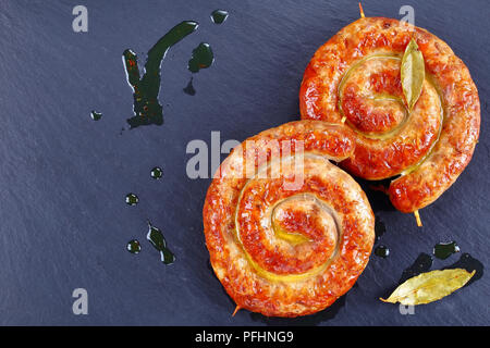 Lecker köstliche deutsche Bratwurst - runde gebratene Würstchen auf Holzspieße auf schwarzem Schiefer Platte mit Lorbeerblättern und heißem Fett Tropfen auf backgrou Stockfoto