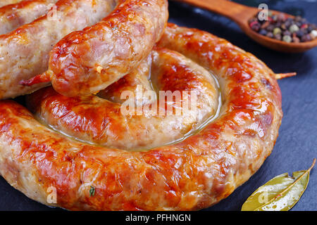 Leckere heiße Englisch Wurst - runde fried Spirale Würstchen auf schwarzem Schiefer Platte mit Pfefferkörnern in hölzernen Löffel auf den Hintergrund, horizontale Ansicht aus Stockfoto