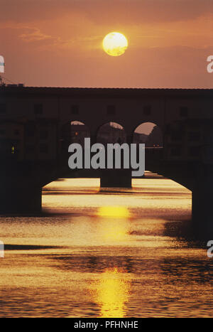 Italien, Florenz, Ponte Vecchio, die untergehende Sonne glühenden über Brücke und Fluss Arno widerspiegelt Stockfoto