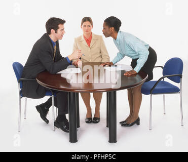 Mann und zwei Frauen, die hitzige Debatte um Tisch, eine Frau, die sich von ihrem Stuhl, Seitenansicht. Stockfoto