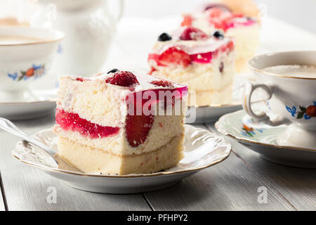 Teile der Käsekuchen mit Erdbeeren, Heidelbeeren und Gelee serviert mit Tasse Kaffee Stockfoto