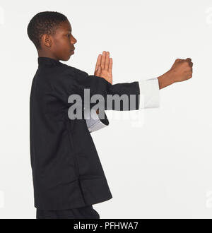 Teenager in Schwarz kung fu Anzug seine rechte Hand nach vorne verlängern in der Faust und biegen seinen linken Arm mit vertikalen Finger vor ihm, Seitenansicht Stockfoto