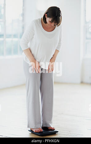 Schwangere Frau im Schlafanzug auf Skalen, die auf der Suche, Ansicht von vorne Stockfoto