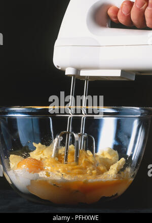 In der Hand gehaltenen elektrischen Mixer rühren, Eier, Mehl und Butter in Glasschale, Seitenansicht. Stockfoto