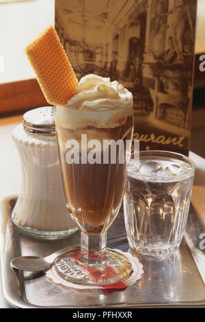 Österreich, Wien, Schokolade Milchshake garniert mit Sahne und einem Wafer in Dessert Glas, ein Glas Wasser und Salz, Shaker, alle auf Metall Fach, aus der Nähe. Stockfoto