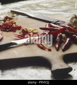 Ganze und gehackte rote Chilis auf einer hölzernen Schneidebrett mit einem scharfen Messer, Seitenansicht. Stockfoto