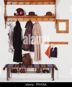 Holz- Mantel und Hut Rack mit Regalen, Hüte und Helm im Regal, Mäntel und Buggy hängen an Haken, Spiegel an der Wand hängen, Schuhe platziert im Regal unter der Sitzbank, Vorderansicht. Stockfoto