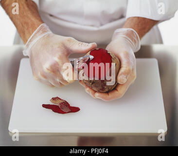Gummihandschuhe zu tragen und mit einem sparschäler Haut von einem Rote Beete abzuziehen Stockfoto