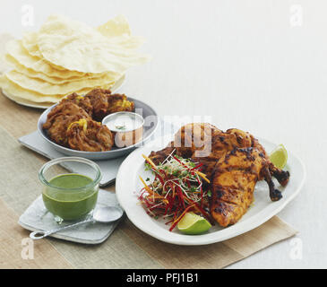 Tandoori Chicken, Gurken dip (raita) und frittierte Zwiebeln bhajis und ein Stapel von popadoms Stockfoto