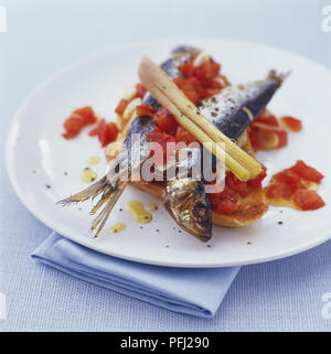 Scheiben knusprigem Brot, mit gehackten Tomaten, zwei gebratene Sardinen und Stiele Zitronengras Stockfoto