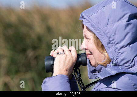 Eine Frau in einem Hooded, Lavendel, Jacke hält Fernglas bereit, während die Vogelbeobachtung. Zum Beispiel: Leonabelle Turnbull Birding Center in Port Aransas, Texas USA. Stockfoto