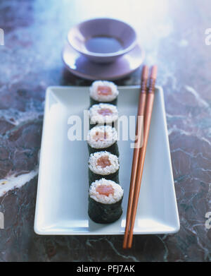 Fünf sushi Pakete auf rechteckige Platte mit Stäbchen, kleine Sauce Schüssel, aus der Nähe. Stockfoto