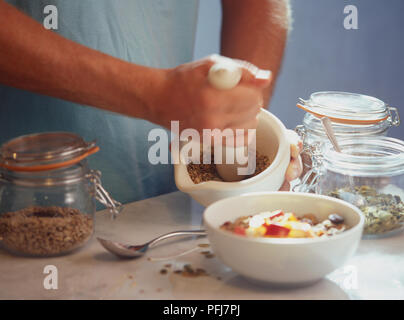 Müsli Mischung, Boden in Weiß Mörser aus Keramik mit Schalen umgeben und Gläser mit Getreide, Obst und Kürbiskerne auf Küche Arbeitsfläche Stockfoto