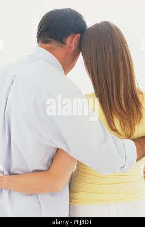 Stehende Mann im weißen Hemd und Frau in Gelb top mit Arm um einander und Köpfe zusammen lehnend, Ansicht von hinten. Stockfoto
