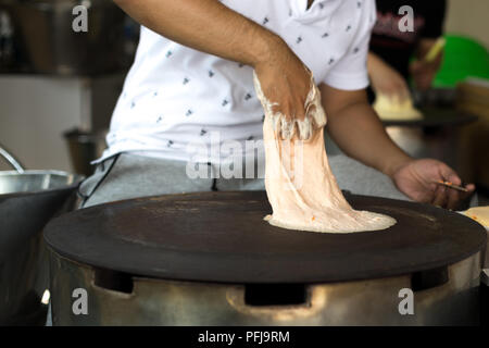 Mann, der ein Roti Teigband auf einer heissen Pfanne Stockfoto