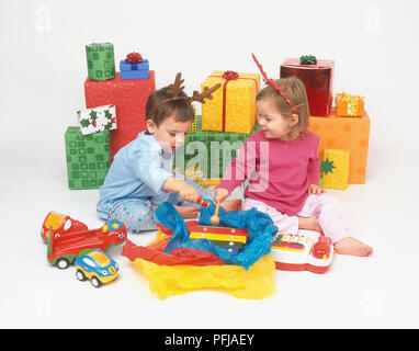 Zwei Kinder sitzen vor dem Haufen Geschenke auspacken ein Xylophon Stockfoto