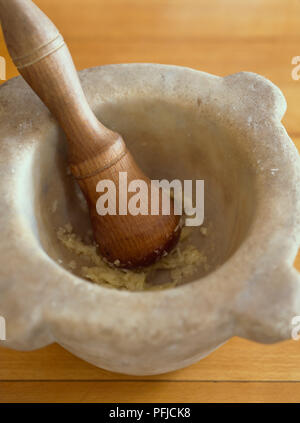 Zerdrückten Knoblauch in Stein Mörser Schüssel mit Holz Mörser, Nahaufnahme, hohe Betrachtungswinkel Stockfoto