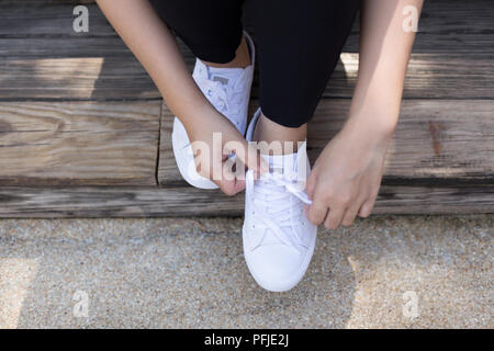 Junge Frau Riegel Schnürsenkel auf weißen Turnschuhen auf hölzernen Deck Stockfoto