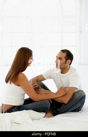 Junges Paar sitzen zusammen auf dem Bett, Hände halten Stockfoto