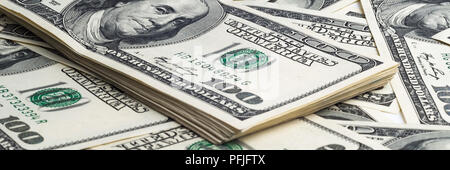 Ein Paket mit einem Hundert-euro-Scheine im Hintergrund der zerstreuten Dollar. Anzeigen in einem Winkel Stockfoto