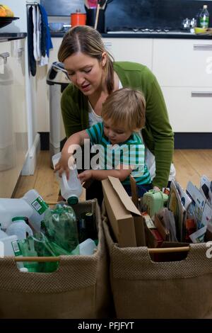 Junge Inverkehrbringen Kunststoff Milchflasche im Recycling Warenkorb auf Küche, Frau beugte sich über hinter ihm Stockfoto