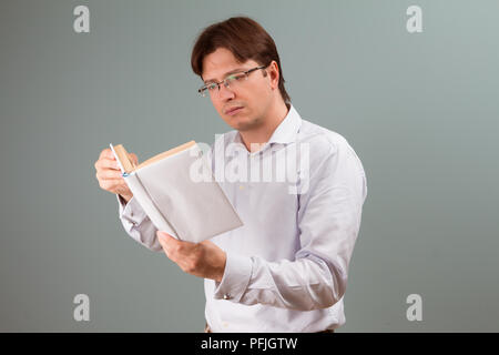 Ein junger Mann, der auf einem Buch in Weiß Abdeckung fokussiert; horizontale Ausrichtung studio Portrait. Stockfoto