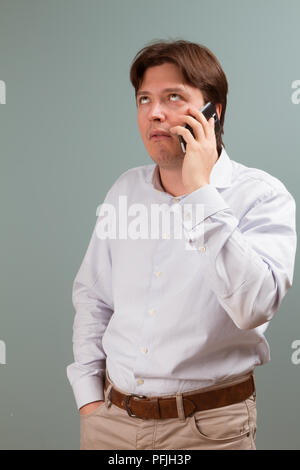 Ein junger Mann schaut auf den Bildschirm seines Handys mit Ausdruck der Langeweile auf seinem Gesicht; Studio Portrait mit grauem Hintergrund Stockfoto