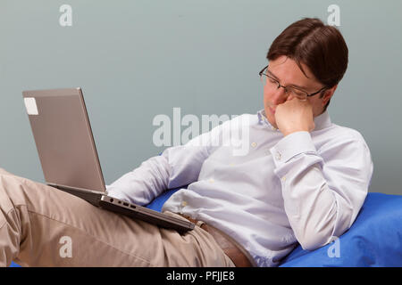 Junger Mann sitzt im Sofa und Arbeiten am Laptop, Einschlafen Stockfoto